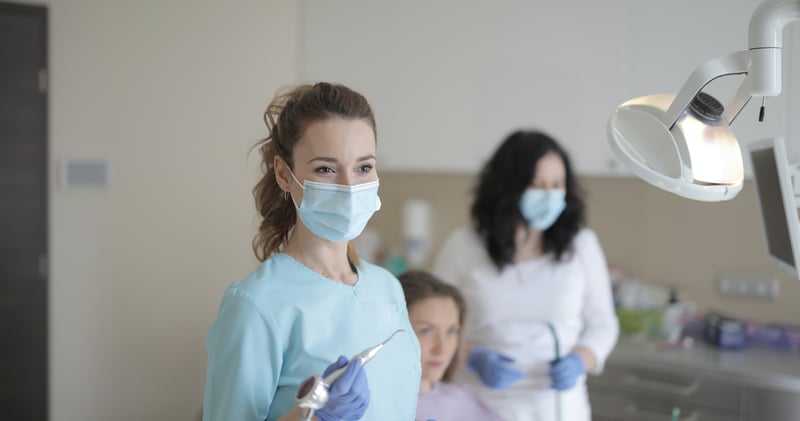 Young female dentist working with assistant while treating patient in modern hospital
